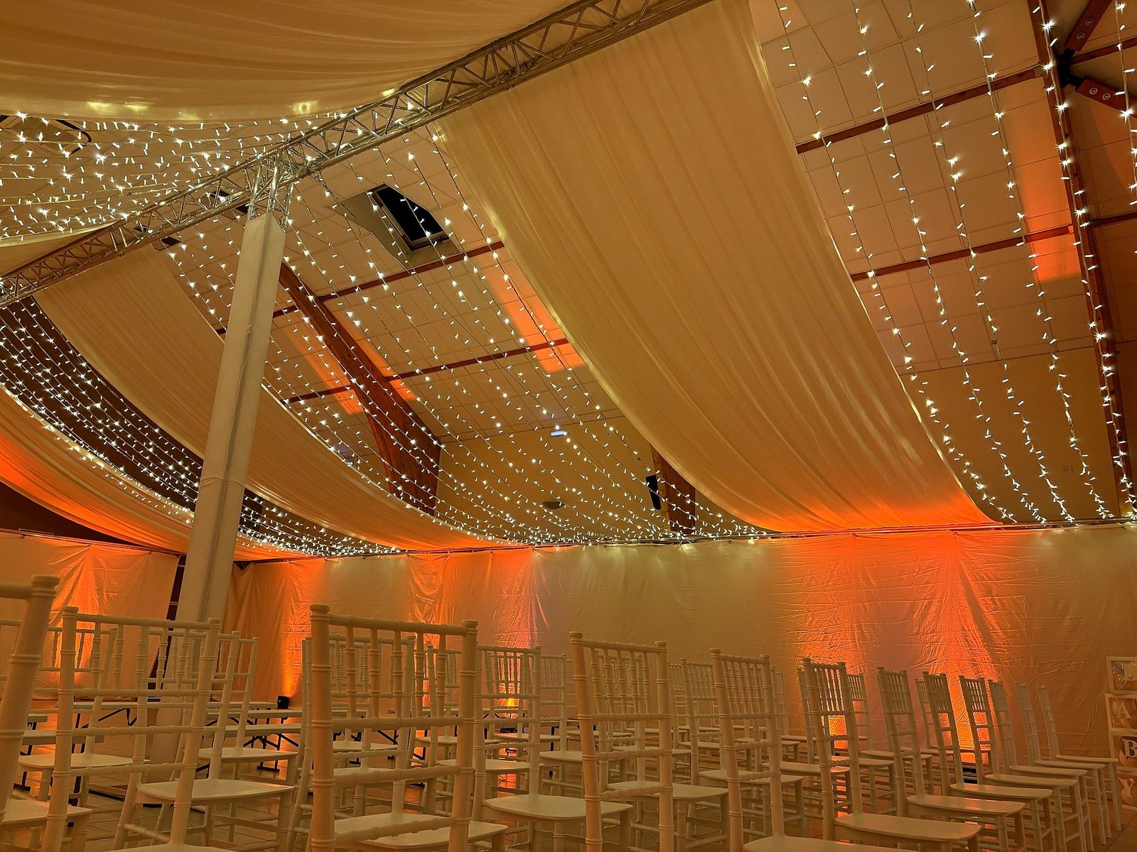 Ambiance chaleureuse sous chapiteau avec voile tendu, guirlandes et éclairage orangé, décoration BLK Production