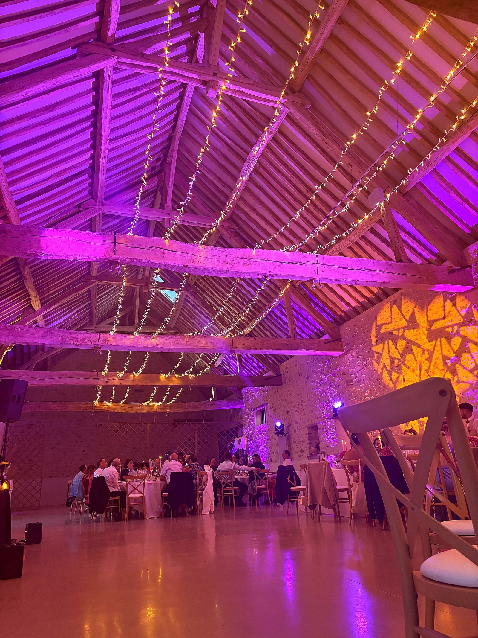 Effet ciel étoilé avec guirlandes tendues entre les poutres d'une charpente en bois apparente, éclairage violet et orange, décoration BLK Production