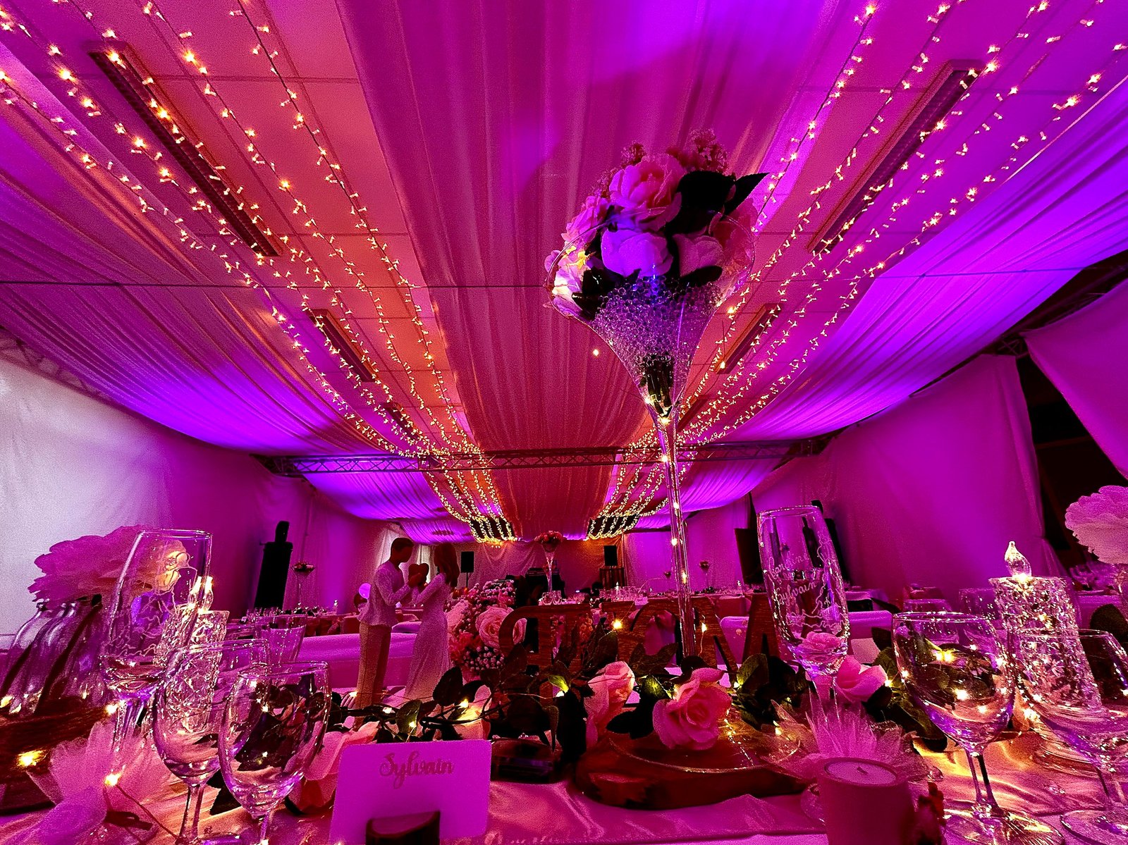 Table dressée avec centre de table élégant sous un drapé lumineux rose et violet, décoration de mariage BLK Production