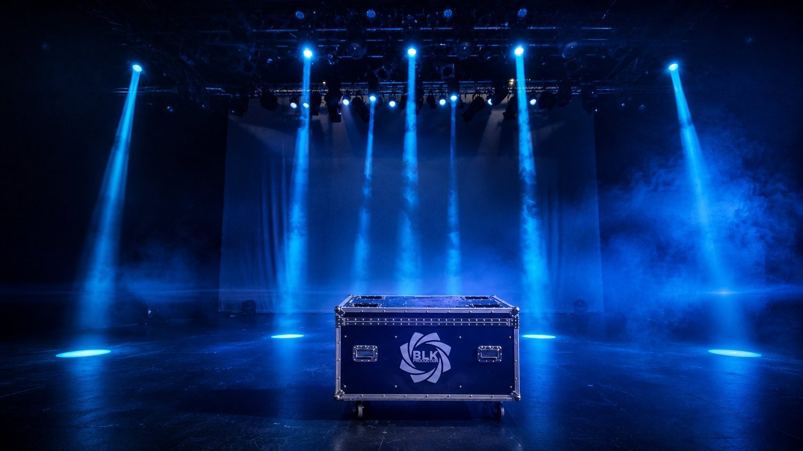 Mise en scène lumière signée BLK Production, six lyres asservies installées sur structure aluminium projettent des faisceaux bleus nets matérialisés par la fumée scénique, flightcase BLK Production au centre de la scène avec logo visible, rideau de fond blanc, ambiance théâtrale