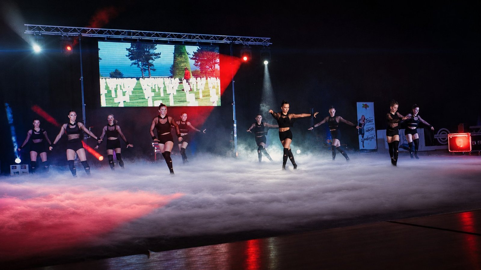 Gala de gymnastique rythmique AGTGR Avant-garde Troyes : neuf danseuses en costumes noirs sur scène, dansent au milieu d'un épais tapis de fumée lourde, faisceaux rouges et blancs, écran LED en arrière-plan diffusant une vidéo mémoriel, structure aluminium scénique par BLK Production