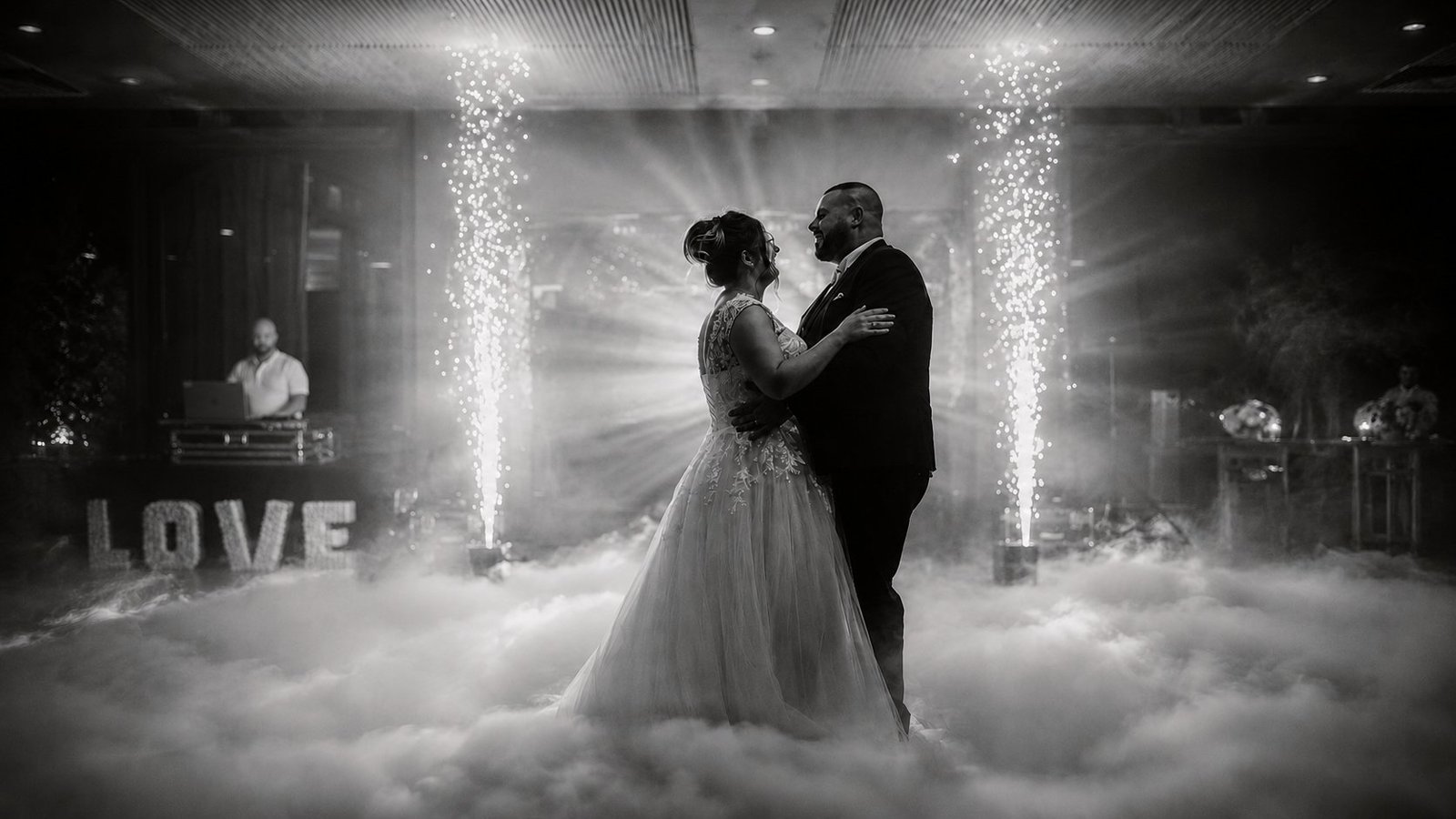 Ouverture de bal de mariage signée BLK Production en noir et blanc, les mariés Nolwenn et Antony enlacés au milieu d'un tapis de fumée lourde, deux jets d'étincelles froides illuminent la scène, lettres lumineuses LOVE à gauche et DJ Flavien Lebel en arrière-plan derrière sa régie