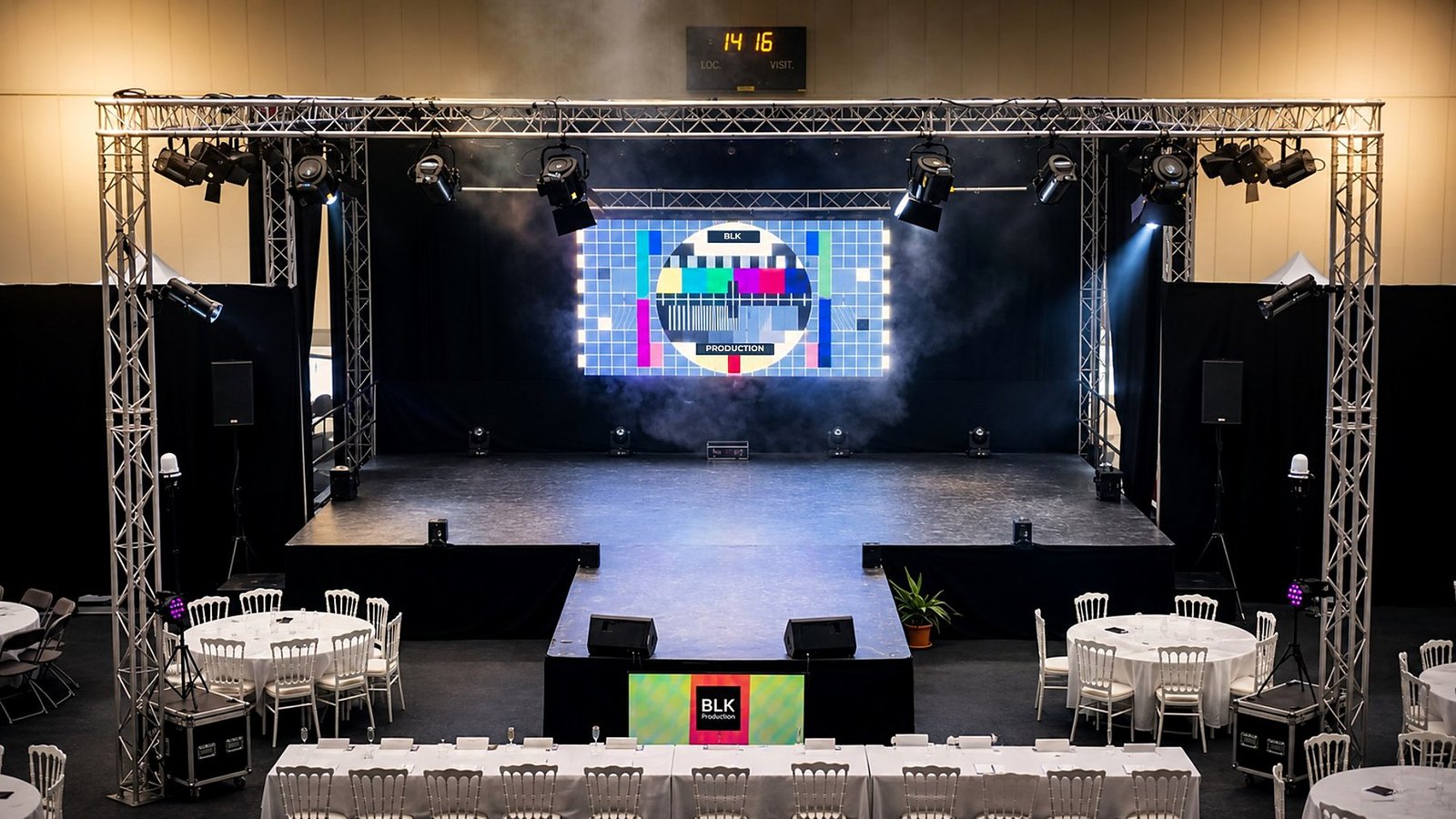 Scène événementielle BLK Production complète : praticable, structure aluminium Global Truss, écran LED central, pendrillons noirs latéraux, projecteurs scéniques, tables banquet en pied de scène pour gala