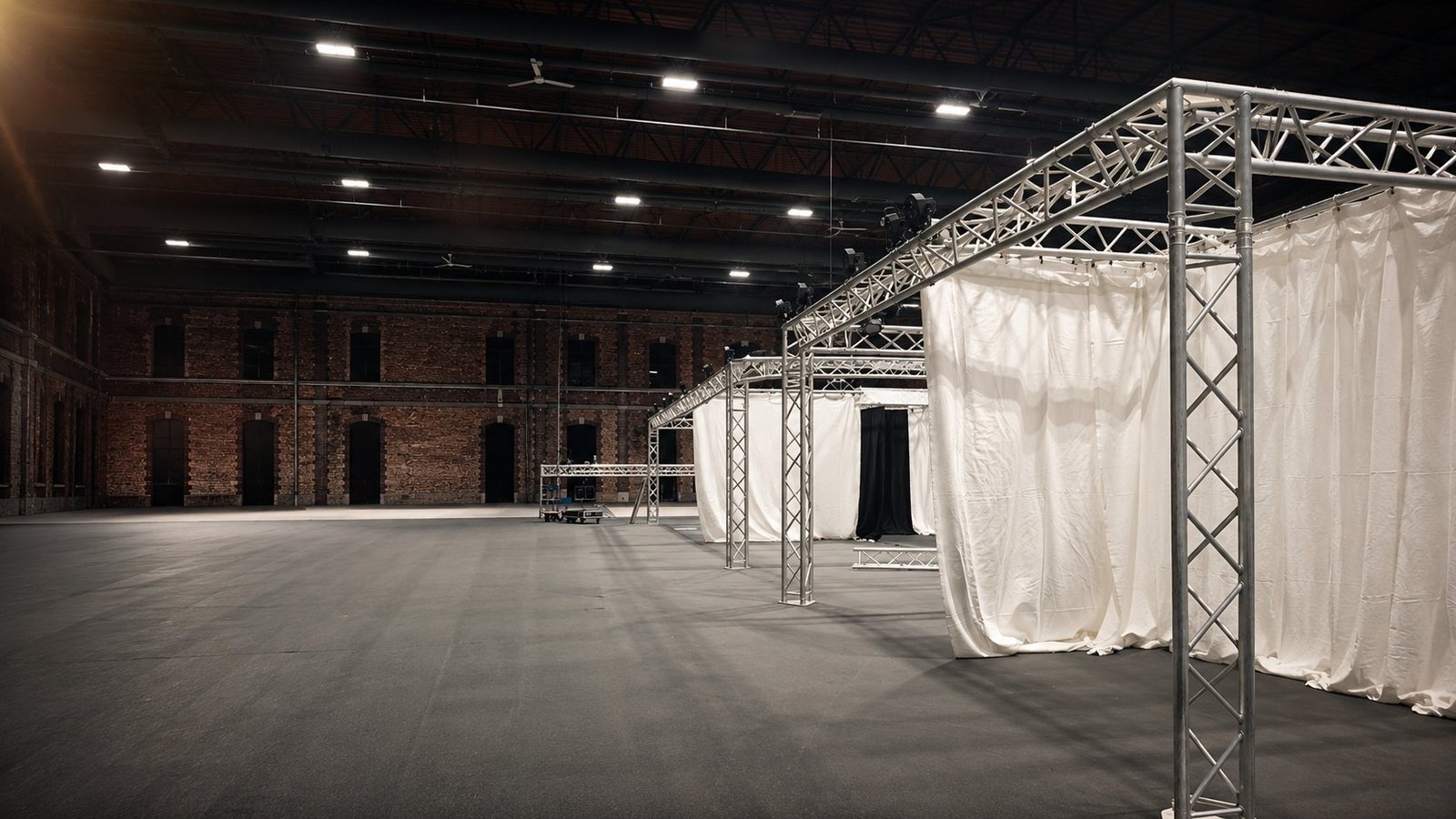 Aménagement de stands modulaires en structures aluminium Global Truss avec tentures blanches et noires par BLK Production pour un salon professionnel, hall d'exposition en brique avec haute charpente métallique