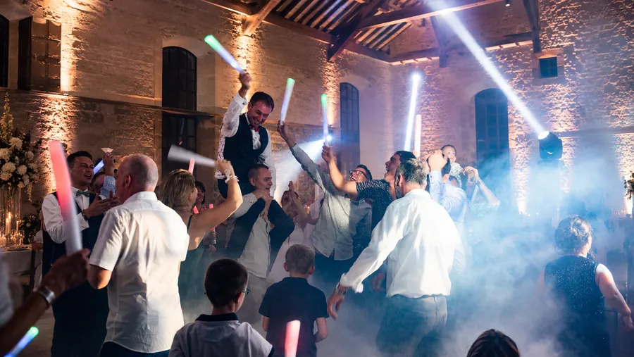 Piste de danse d'un mariage dans une salle en pierre, faisceaux, fumée et bâtons lumineux