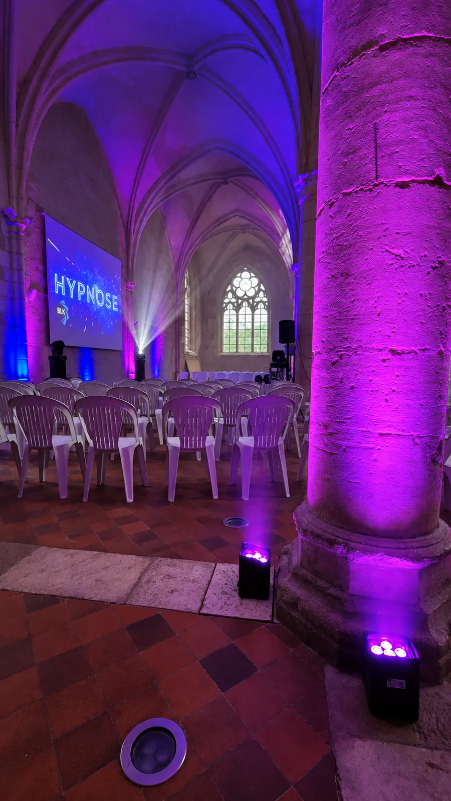 Salle voûtée mise en lumière en violet et bleu par des projecteurs sur batterie, pour un spectacle d'hypnose