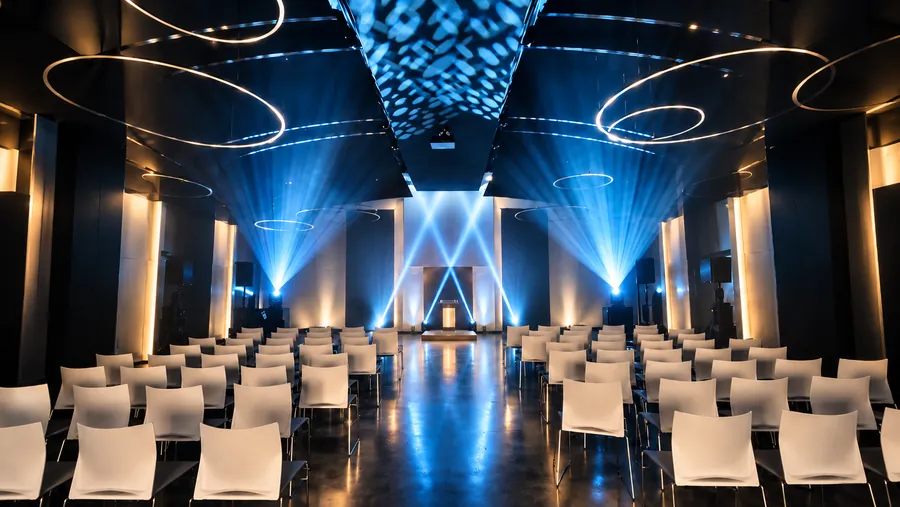 Salle de spectacle préparée pour le Crédit Agricole, rangées de chaises blanches, faisceaux bleus croisés et gobos au plafond