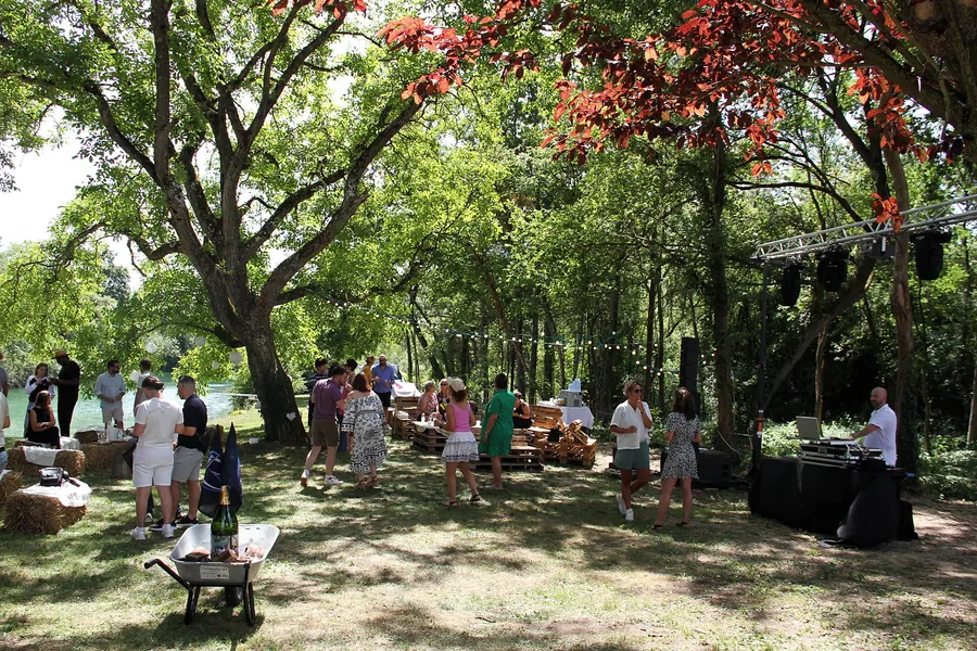 Invités sous les arbres au bord de l'eau, structure et régie DJ sur la droite