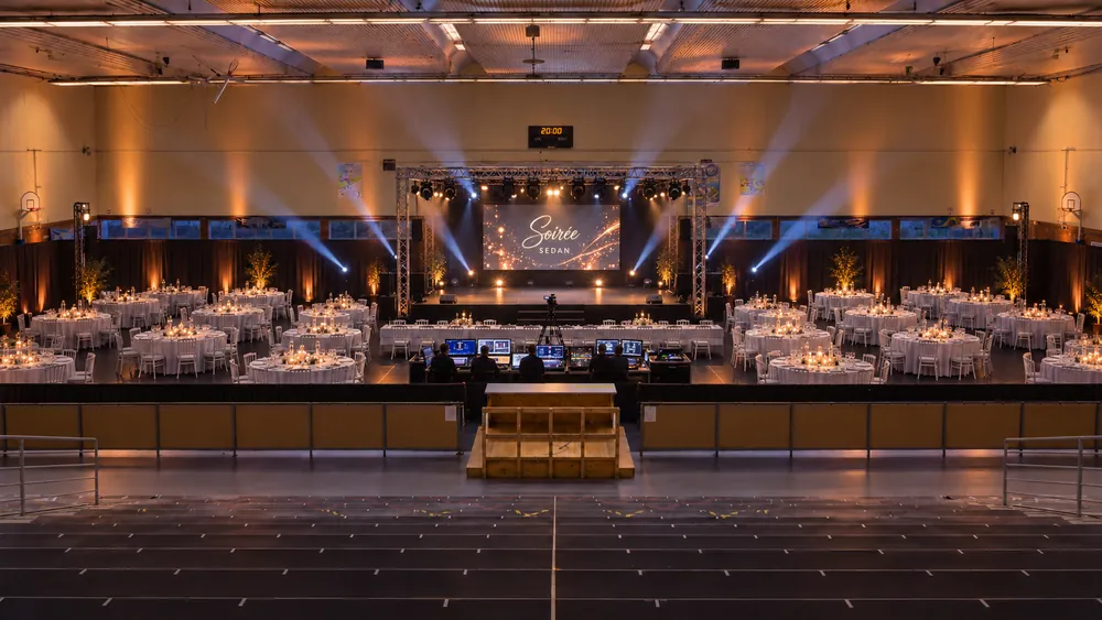 Gymnase transformé en salle de gala : scène, écran LED, faisceaux et tables dressées